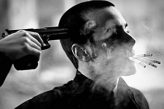 Мужчина с сигаретами во рту под дулом пистолета